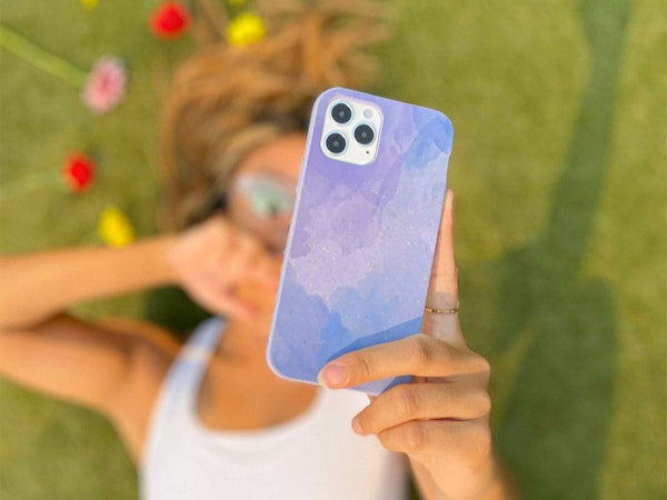 A woman holding her phone in a lavender blue reflections Pela case
