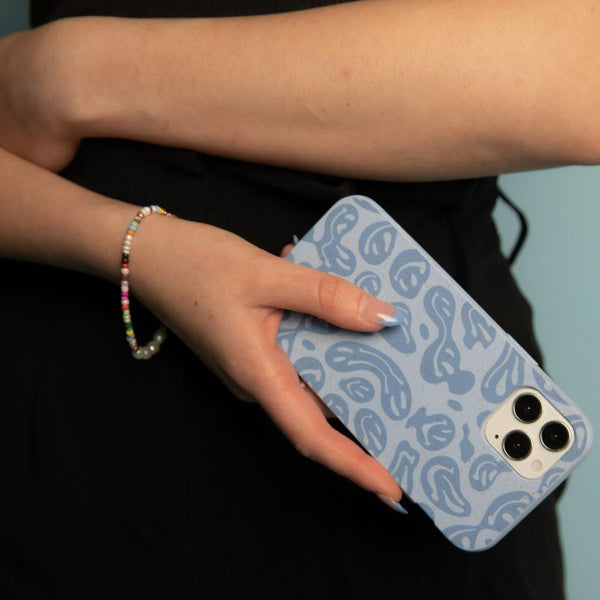 A woman holding her phone in a powder blue melting faces Pela case