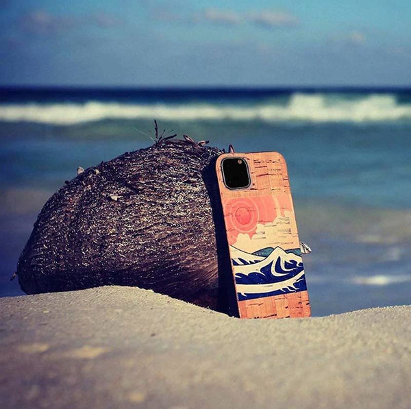 A cork phone case with a wave print resting on the beach