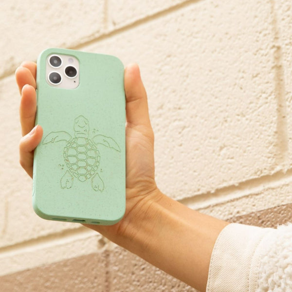 Hand holding turquoise ocean turtle phone cover by brick wall