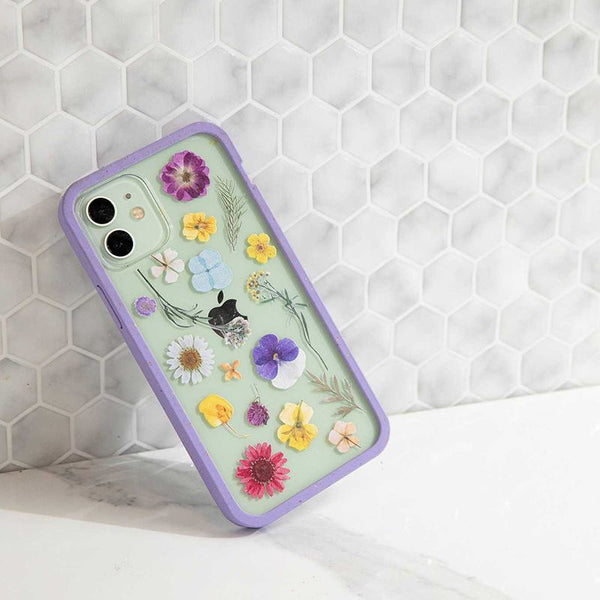A clear phone case with pressed flowers leaning against a wall