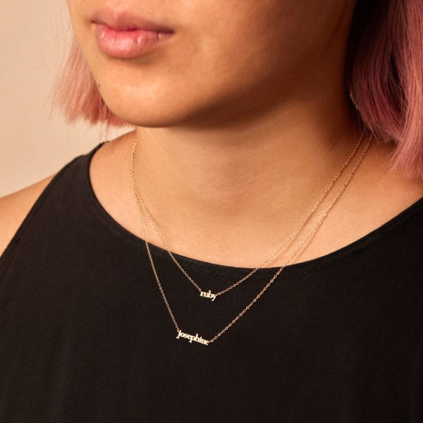 A close up of a woman wearing recycled gold necklaces that say ruby and josephine