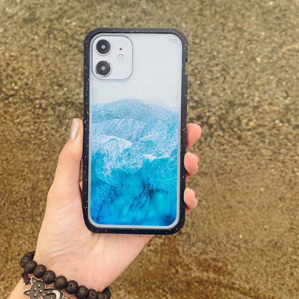 A hand holding a phone with a wave printed on it over sand