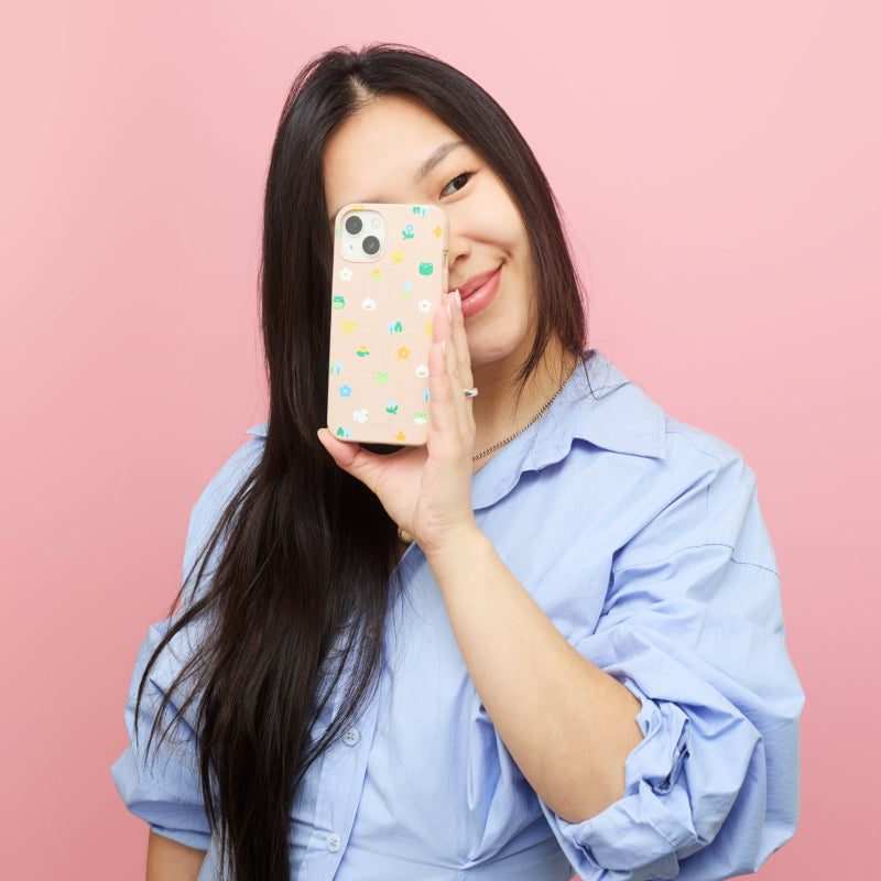 Smiling woman covering half of her face with a patterned smartphone case against a pink background.