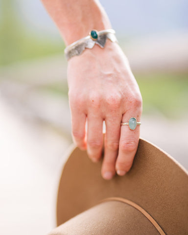 Woman holding hat wearing mountain inspired jewelry 