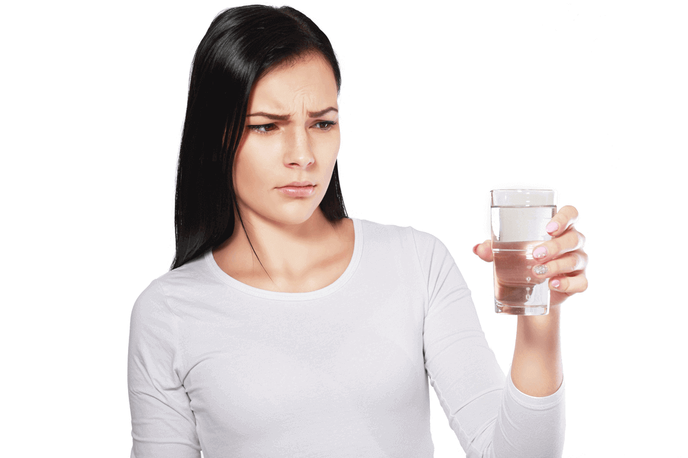 A female looks doubtful to the glass of water she’s holding