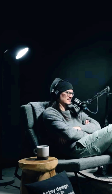 Man sitting on a couch, talking, with surfboards and a light setup in the background.