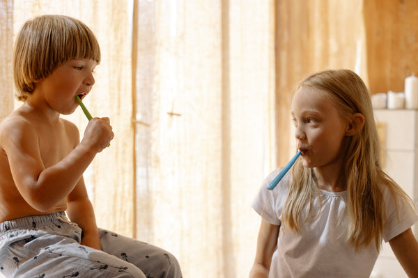 blonde girl and blonde boy siblings brushing teeth