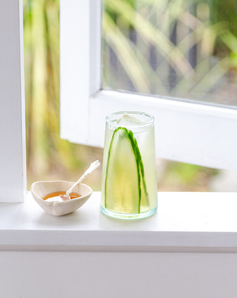 cup of water with cucumber slices and honey white window