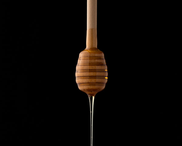 honey dripping off wooden honey spoon black background