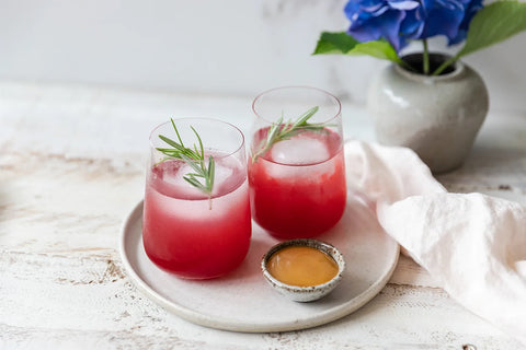 two clear stemless glasses filled with red drink and rosemary garnish