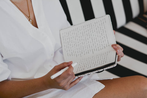 woman in white button up shirt holding white journal and pen