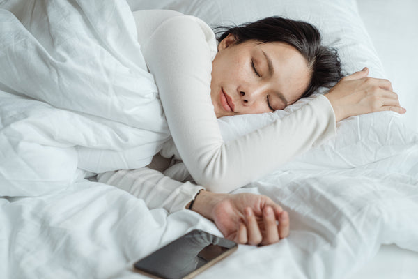 woman with black hair sleeping in bed with white comforter and sheets