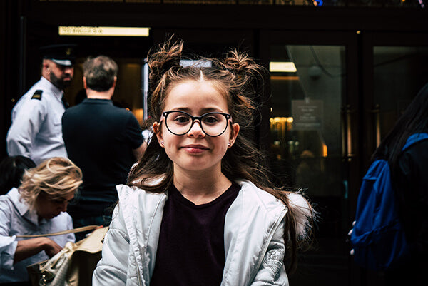 A little girl with glasses is looking into the camera