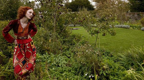Red headed woman wearing 1970s boho vintage dress, standing in an orchard in autumn
