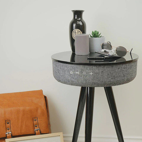 A grey bluetooth speaker table with ornaments and sunglasses on