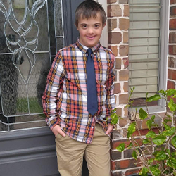 Image of Ry standing infront of a house, wearing a
                checkered shirt and navy blue tie