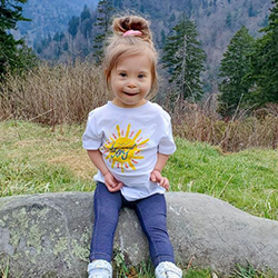 Image of toddler, Ivy, wearing a white shirt with the
                design"Spark Joy" 