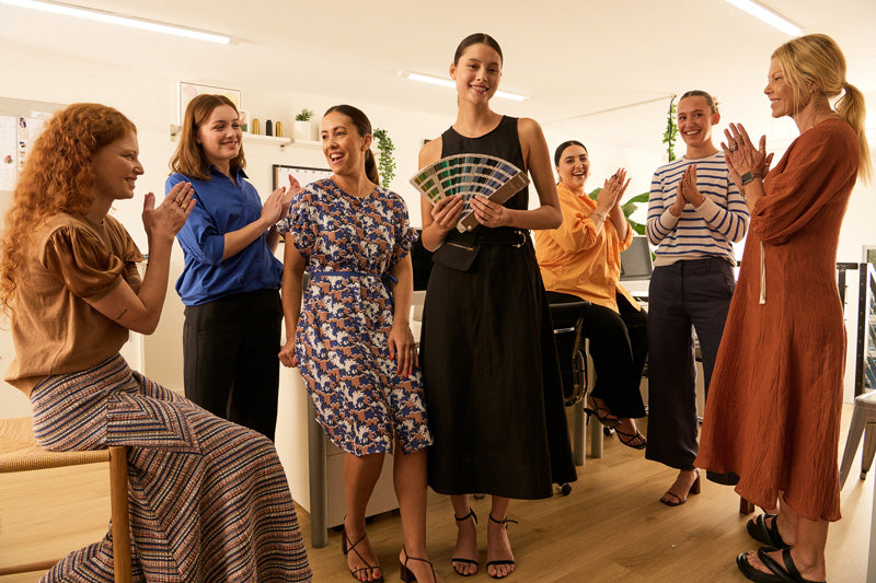 A group of women sit and stand around an office desk