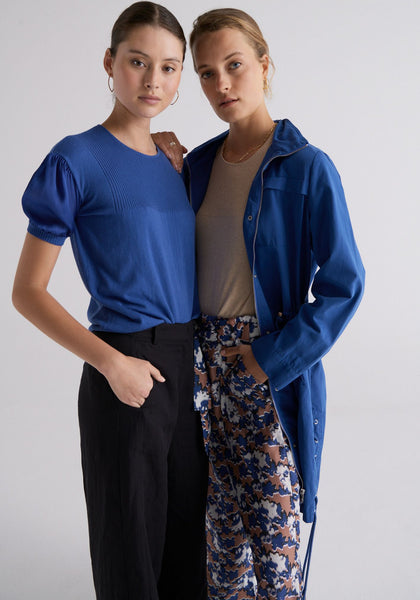 Megumi wears the Kaia Silk Sleeve Tee in Marine and the Riley Pant in Black, and Esti wears the Slone Anorak in Marine over the Kaia Silk Sleeve Tee in Pebble and the Marnie Pants.
