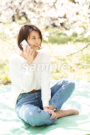 桜の下で電話するあぐらで座る女性の写真 Aph Prismgraph プリズムグラフ