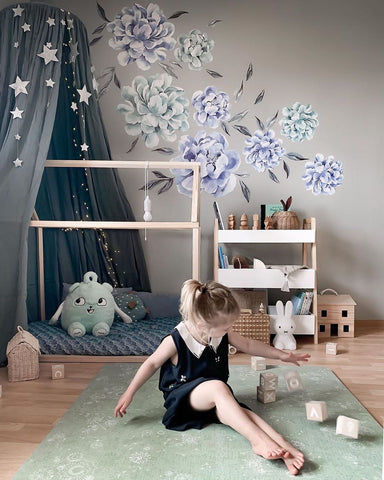 Buntes Kinderzimmer mit Blumentapete und grüner Spielmatte, auf der ein Kind mit Holzspielzeug spielt
