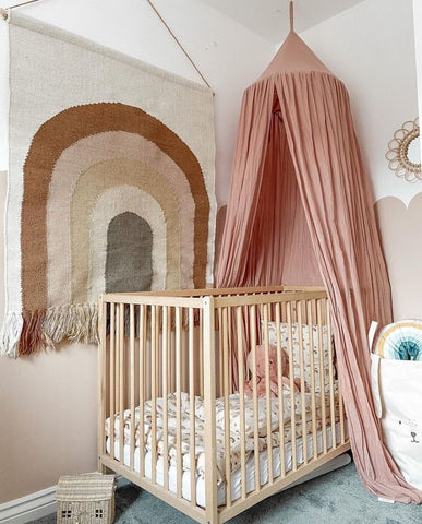 Colorful nursery with tones of pink, a rainbow tapestry and a pink canopy 