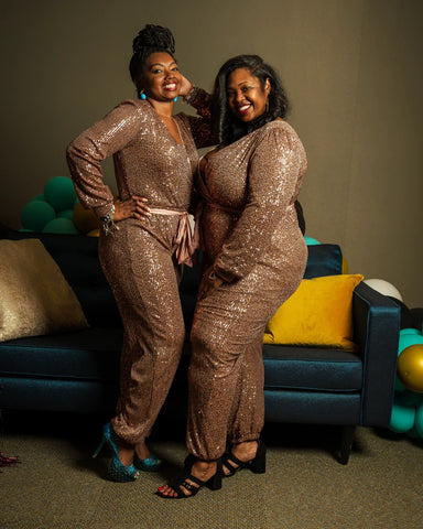 Two models stand in front of a couch wearing the bronze sequin jumper and smiling