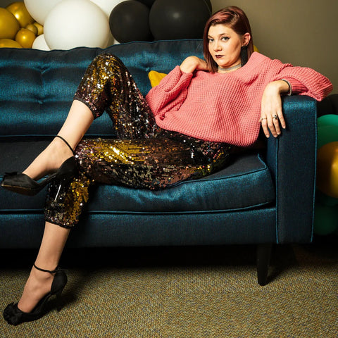 model lounges on a couch wearing black sequin pants and coral colored top