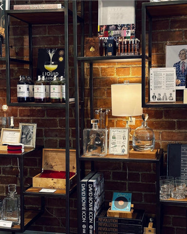 A dark, masculine shelf displays gifts for men including artwork, whiskey, glassware and home accessories from Talulah Belle.
