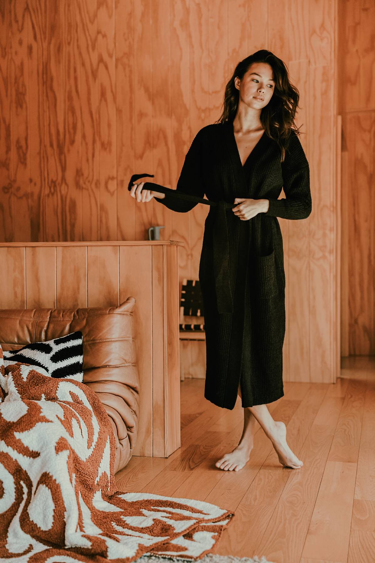 Woman lounging in long cardigan. Ribbed long cardigan. Cozy long black cardigan. Women's cardigans. Woman relaxing at-home in cardigan.