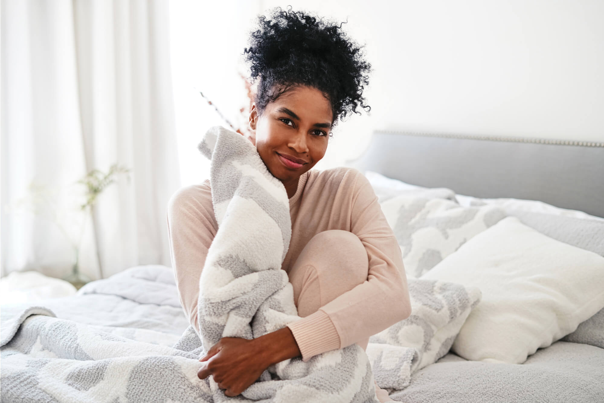 Woman cozied up to snuggly blanket. Woman snuggling cozy blanket. Woman hugging cozy blanket. Woman sitting in bed with cozy blanket. Woman smiling with comfiest blanket.