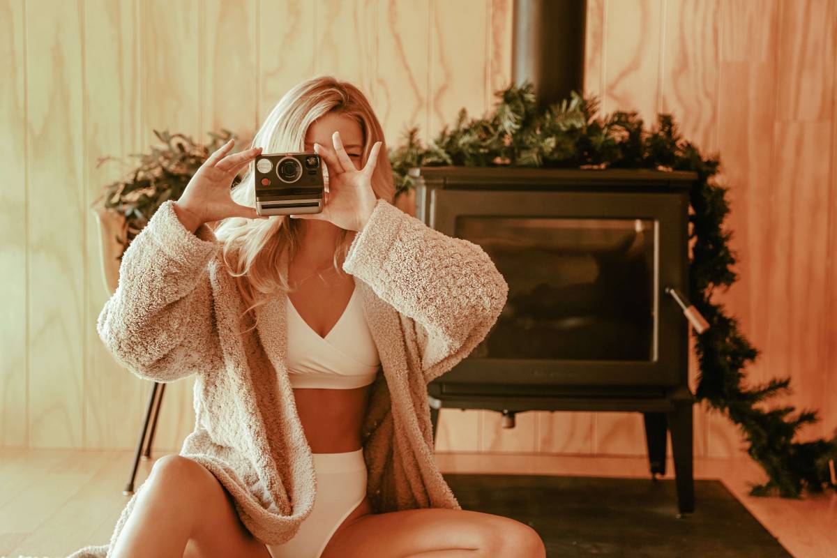 Woman taking a polaroid picture. Woman using polaroid camera. Polaroid pictures at the holidays. Woman in cozy bath robe.