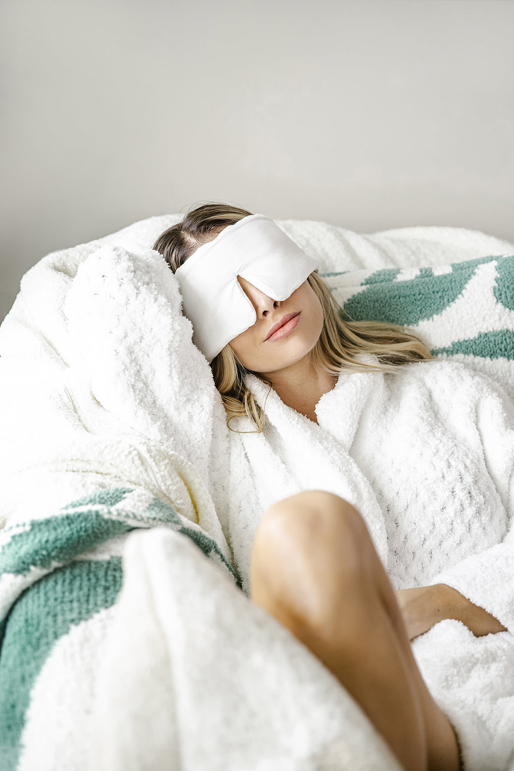 Woman laying down with sleep mask on face and wearing a white bath robe. Woman taking a nap. 