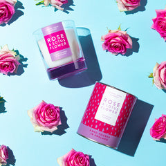 Rose & Lotus Flower Luxury scented candle from Lower Lodge Candles Colour Pop! collection pictured with its cardboard tube packaging against a light blue background with pink rose flowers