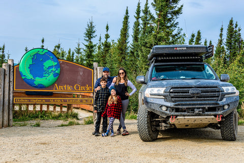 Family standing near their overlanding rig and an Artic Circle sign