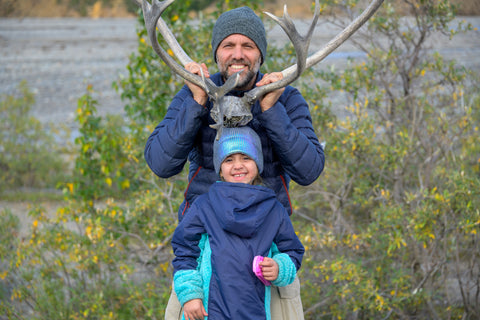 A father stands behind his daughter holding deer antlers behind her head smiling