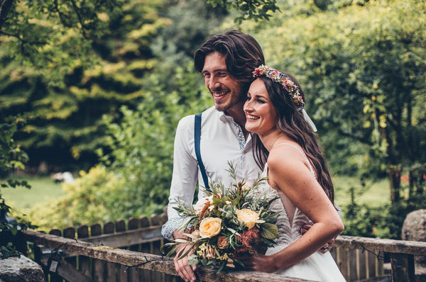 Couple stand in relaxed wedding attire in garden.