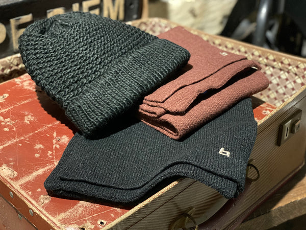 A black beanie is displayed on top of a black soft knit scarf and a wine soft knit scarf.