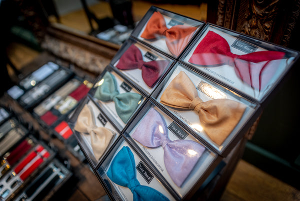 Bow ties on display in shop with braces displayed in background.