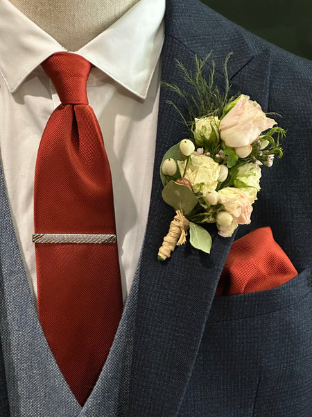 Mannequin dressed with navy men's suit, SUAVE OWL white shirt, a red tie, and a floral boutonniere in pink.
