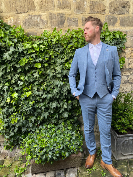 Model wears Wells pale blue suit whilst against a background of ivy and exposed brick.