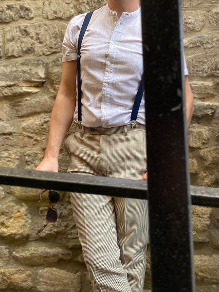 Model wearing the Elwood trousers with brace braces and an off-white short sleeve button up.