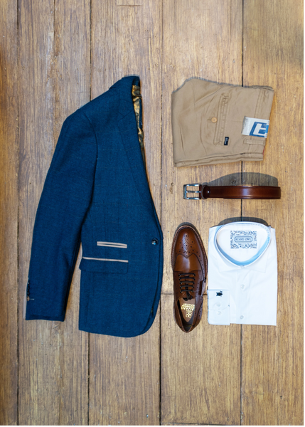 A dion jacket, sand chinos, SUAVE OWL white shirt, brown belt and brogues are laid out on a wooden background.
