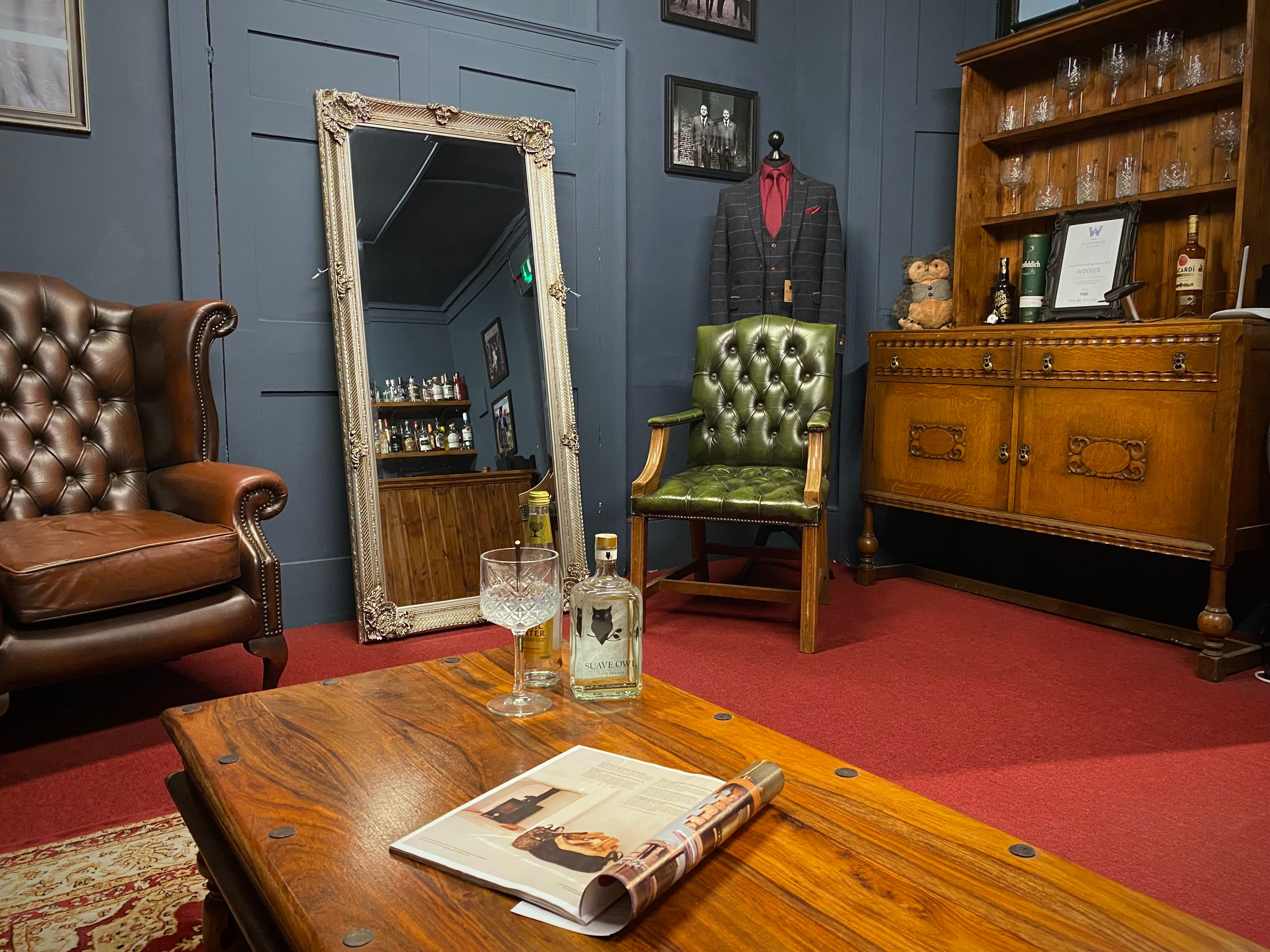 Leather chairs are placed around a grand full-length mirror. The red carpet is adorned with a darker red rug. The furniture is aged wood.