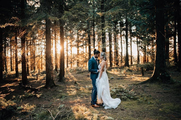 Couple stand in woodland with sun behind.