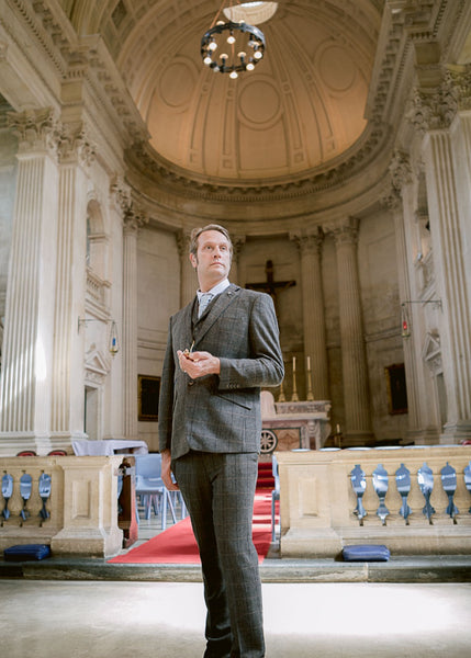 Groom waits anxiously with pocket watch in ornate chapel. 