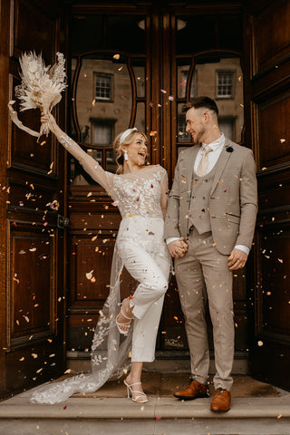 Groom wears a cream suit for men whilst being showered with wedding confetti.