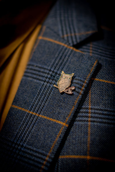 SUAVE OWL lapel pin on a navy men's suit.