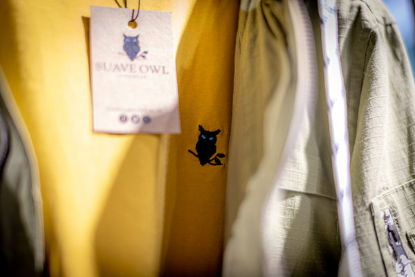 A SUAVE OWL yellow T-shirt with a jacket is displayed on a hanger.